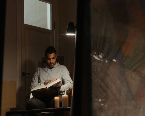 Reading a physical book under a warm reading lamp during a rainy evening